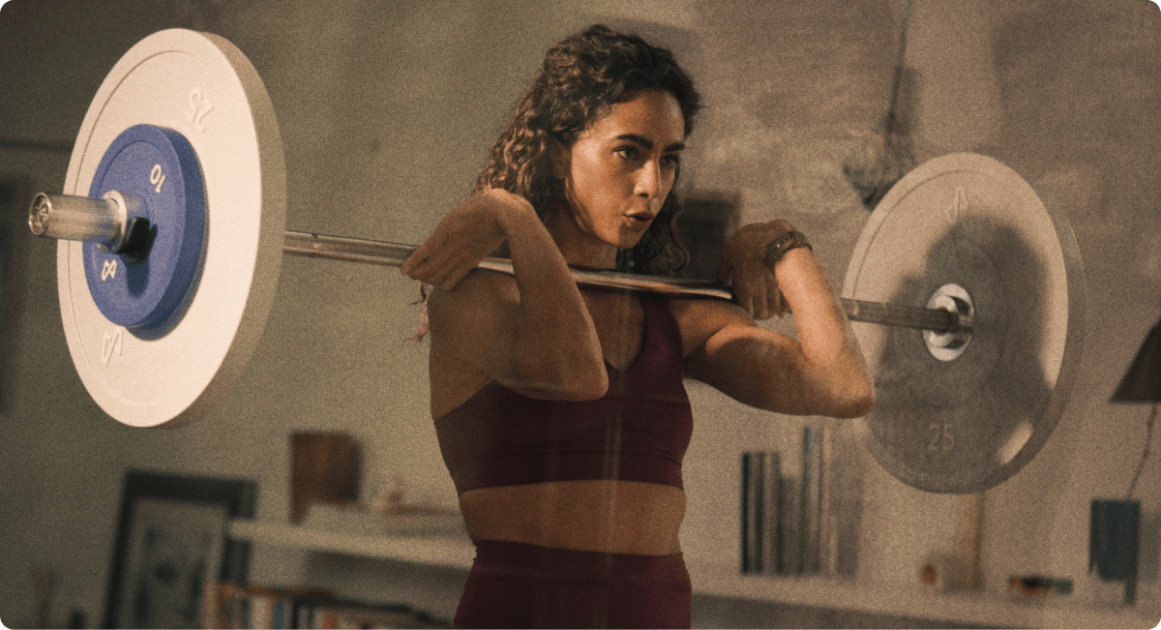 Woman holding a loaded barbell at her shoulders in a home gym